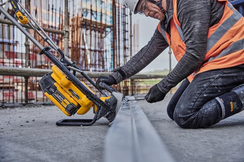 A person wearing construction safety gear uses a DEWALT cordless power tool (SKU: DCPS330N) on a metal beam at a construction site.